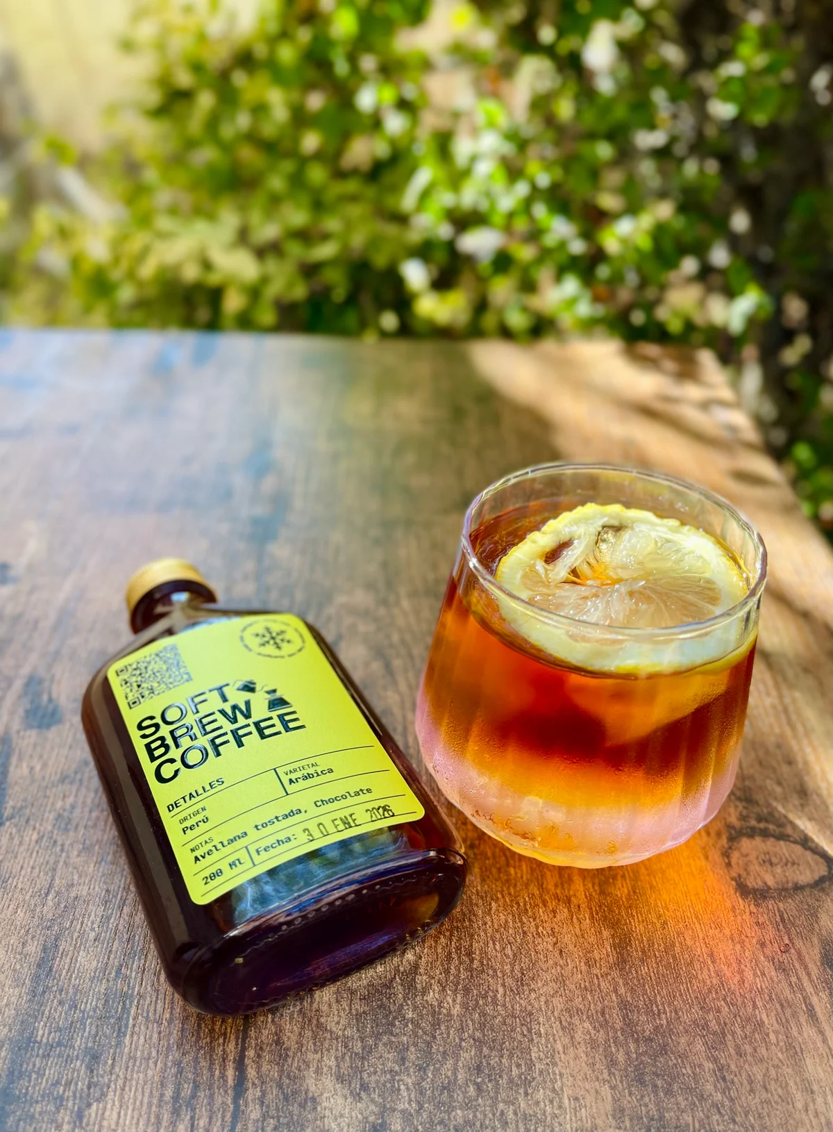 Botellín de Perú junto a un vaso con hielo y una rodaja de cítrico, sobre una mesa de madera
